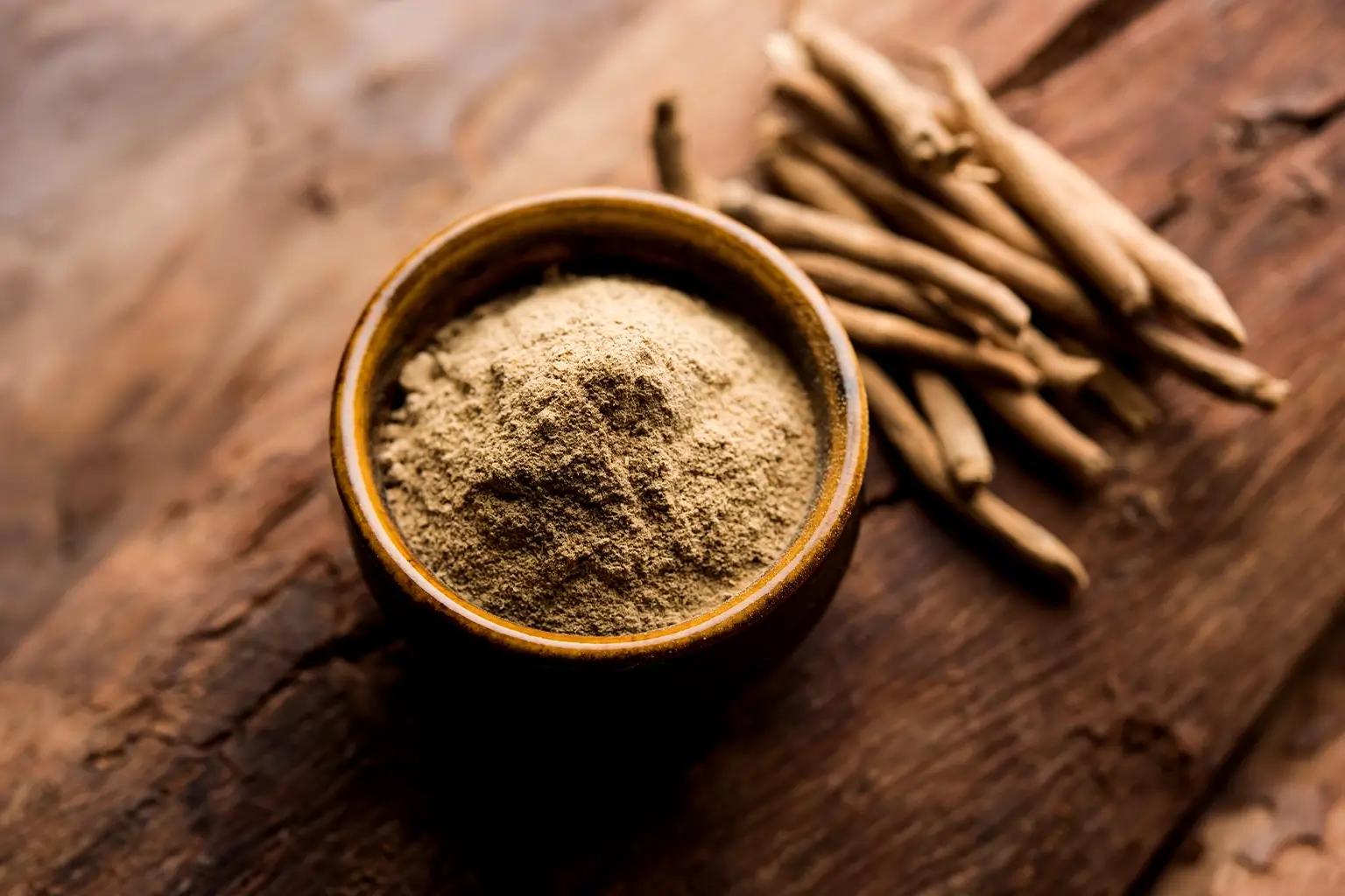 Ashwagandha root powder in a ceramic bowl with dried roots nearby