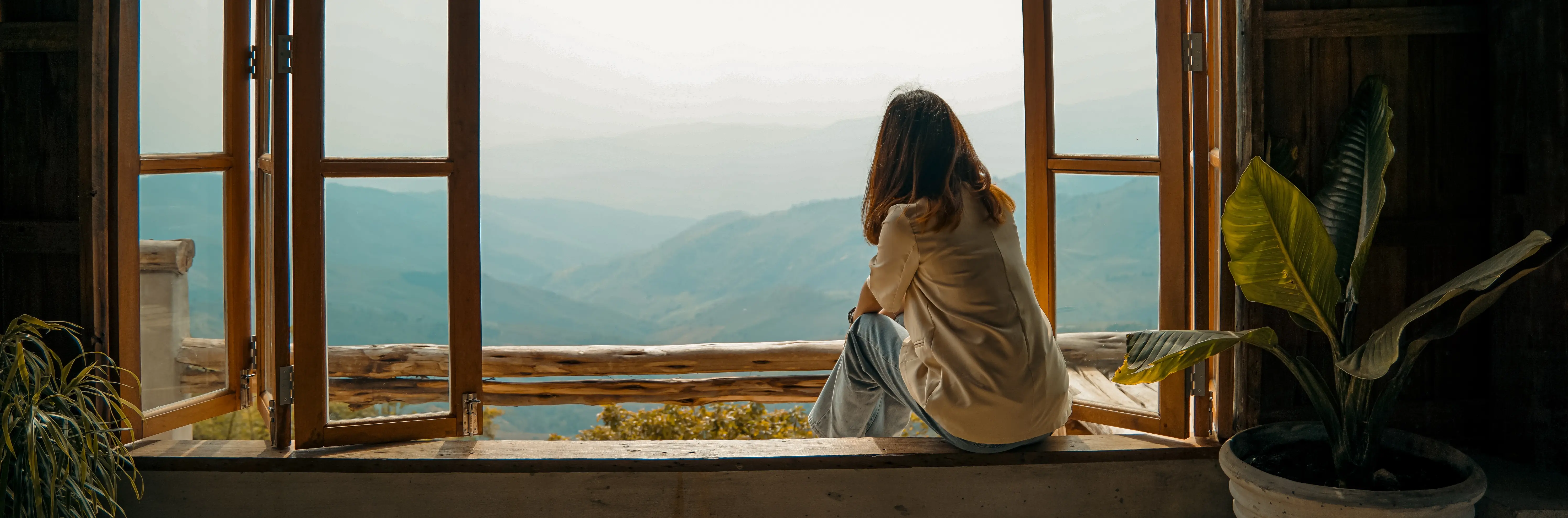 A woman sitting in an open wooden window overlooking misty mountains