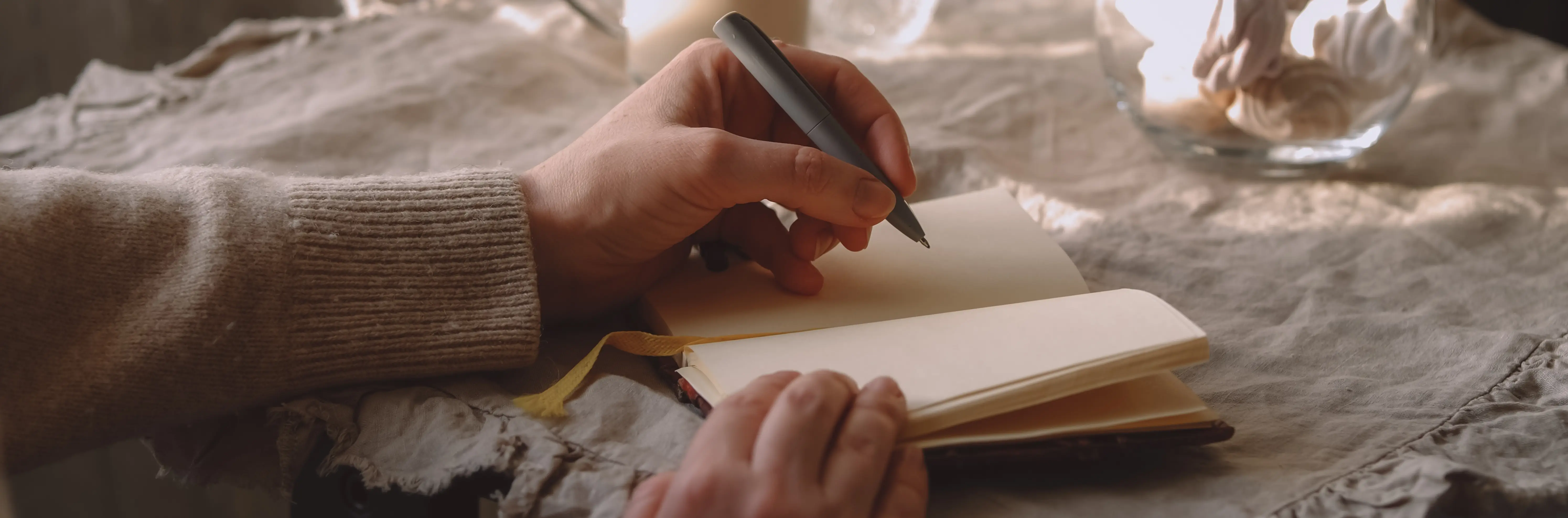 Hands writing in a small cream notebook on a linen cloth